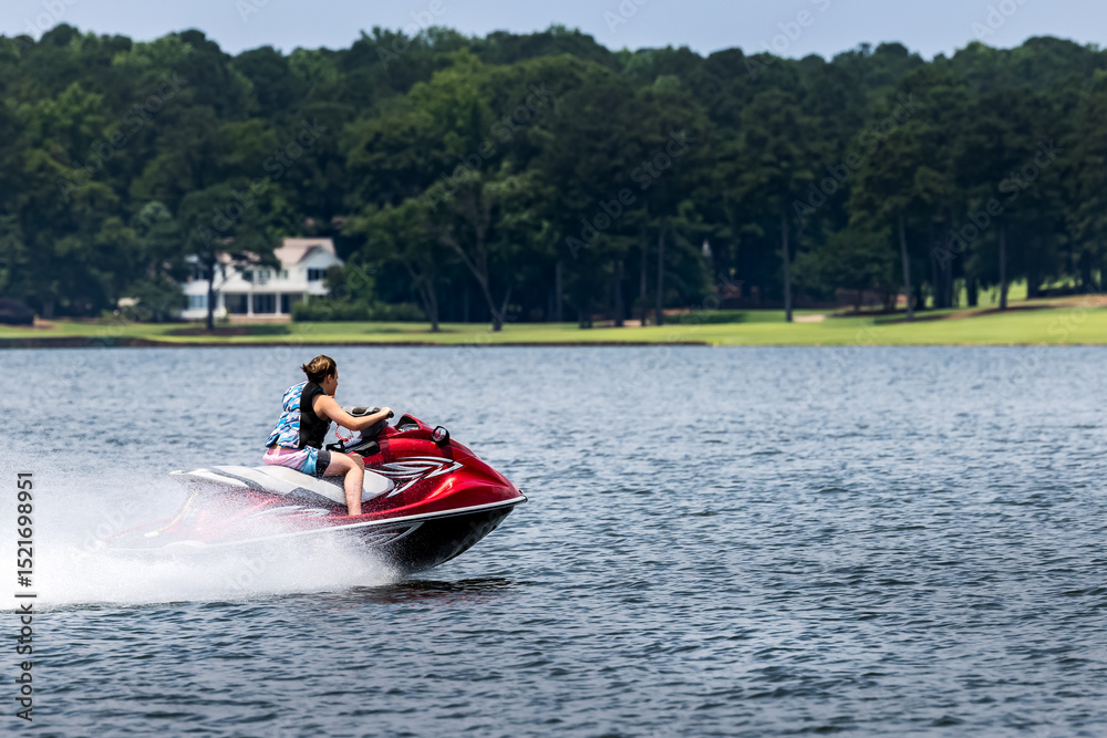 Fototapeta premium Teenage boy riding jet ski personal watercraft and enjoying summer day on lake.