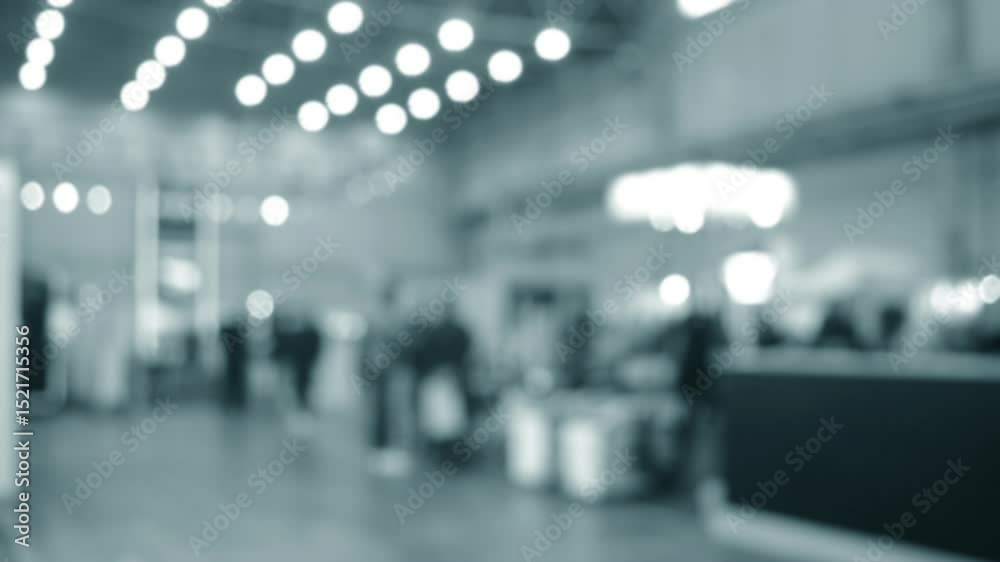People walking in building. Building with walls, floor, ceiling illuminated lamps. Silhouettes of people indoors. Many people walking. Men and women in tall hall. Exhibition center. Blurred background People walking in building. Building with walls, floor, ceiling illuminated lamps. Silhouettes of people indoors. Many people walking. Men and women in tall hall. Exhibition center. Blurred background