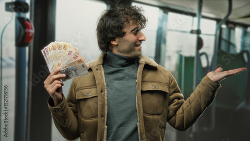 Hispanic man joyfully presenting turkish lira banknotes inside a bus, engaging in an animated gesture, highlighting vibrant economic exchange in indoor urban transit setting.
