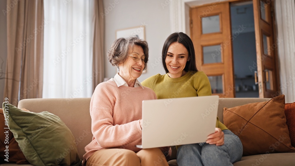 Positive Caucasian grandmother with her daughter or granddaughter using laptop. Women talking by videocall with their family members. Waving hands to camera while ending conversation. Positive Caucasian grandmother with her daughter or granddaughter using laptop. Women talking by videocall with their family members. Waving hands to camera while ending conversation.