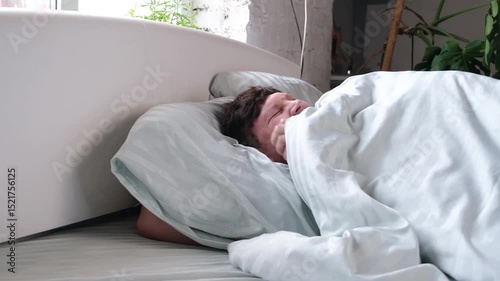 Young millennial man sleeping looking at screen mobile phone smartphone lying in the bed in the morning