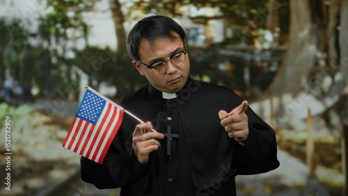 Young man dressed as priest holding american flag in a park setting, blending religious symbolism with national identity in an outdoor environment.