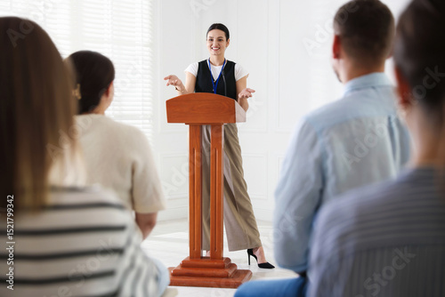 Quadro em tela Woman giving public speech at lectern in front of audience indoors