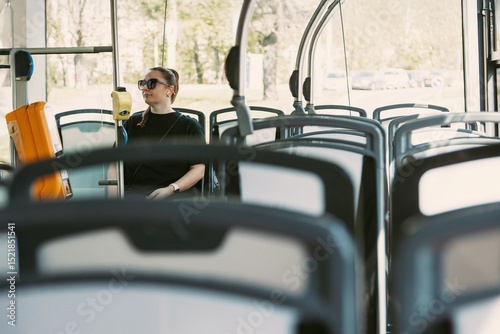 A young woman with sunglasses rides a modern city bus in solitude. Ideal for projects on urban commuting, public transportation, daily routines, and quiet travel moments.