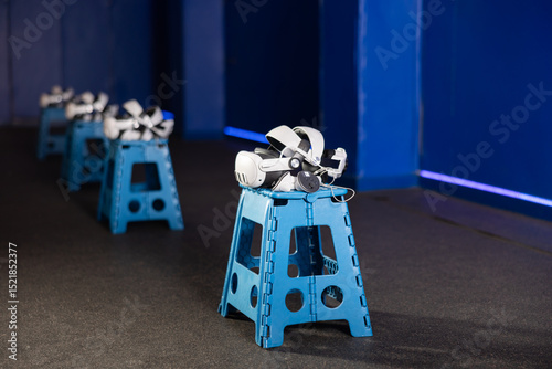 Fototapeta Naklejka Na Ścianę i Meble -  VR headsets and controllers arranged on stools in gaming room with modern, minimalist design and blue lighting creating futuristic ambiance, ready for immersive virtual reality experience