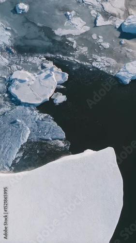 Aerial perspective of floating ice formations in a frigid glacial body of water, glistening in the sunlight