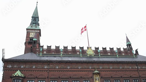 Copenhagen city hall building with a danish flag waving in the wind on the top. Main touristic spot of danish capital in the city center with the political symbol of the country.