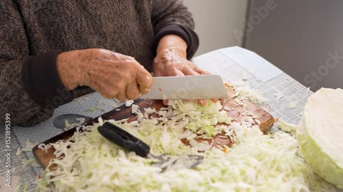 Close-up of elderly hands using a cleaver to efficiently shred cabbage. The process highlights traditional cooking skills and meticulous techniques in food preparation at home 