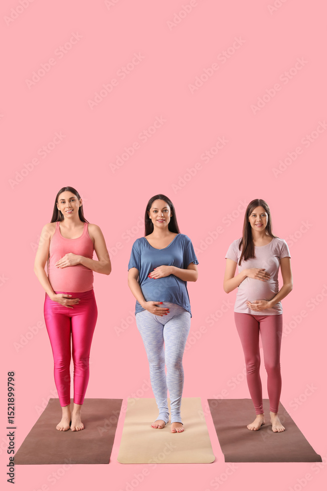 Fototapeta premium Beautiful young sporty pregnant women practicing yoga on pink background