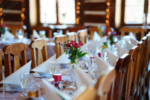 Bild auf Leinwand Elegantly set wedding table with flower decorations, champagne glasses, and folded napkins in a cozy wooden interior with warm fairy lights