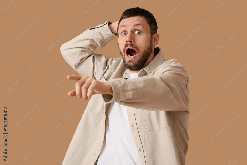 Fototapeta premium Shocked young man pointing at something on beige background