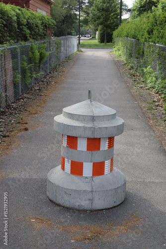 A cement block whit orange sign for slow down the speed and for mark a road divider. Path and road for bicycle or pedestrian. Concrete lane separator.
