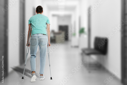 Man with axillary crutches in hospital, back view. Space for text
