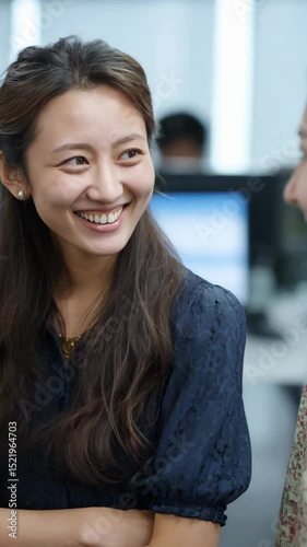 Cheerful young business woman smiles while having a conversation with a colleague in a modern office environment indoors.