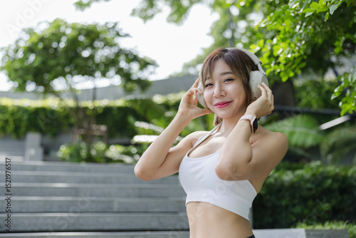 A young woman enjoys music in a vibrant urban park while wearing headphones, showcasing her confidence and happiness, embodying an active and engaging lifestyle in nature. photo
