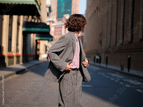 Portrait of handsome Chinese young man wearing gray suit looking back in the street, young guy with black curly hair with urban background. Male fashion, cool Asian young man lifestyle.