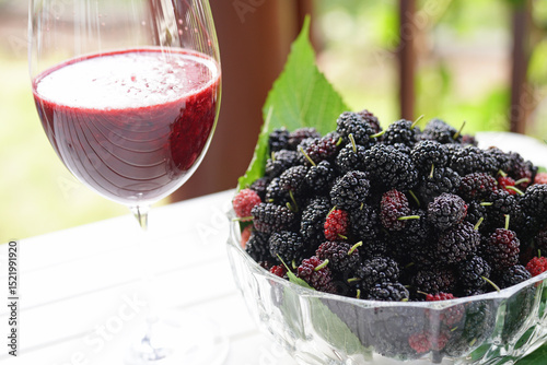 Mulberries in glass bowl with glasses of mulberry juice.