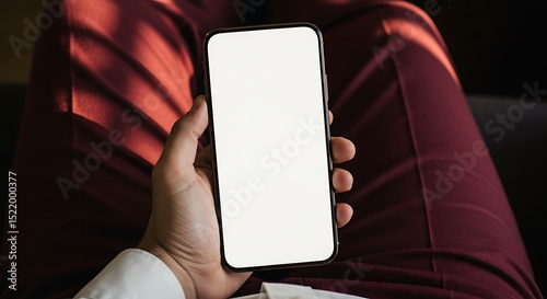 Person holding smartphone with blank screen mockup against maroon fabric background ideal for app presentations and website design