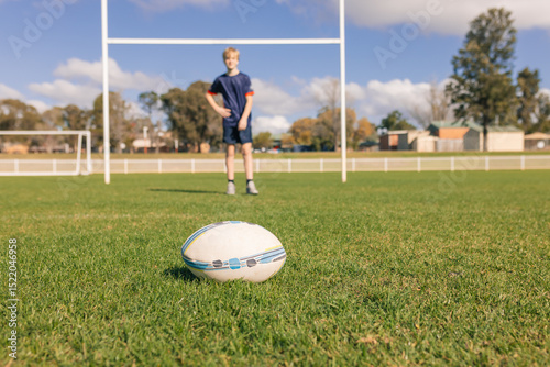 Rugby ball on field with player and goal posts in background