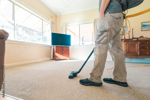 Professional man vacuuming carpet in home in preparation for steam cleaning