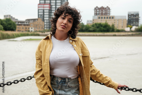 Young woman posing by a chain fence in an urban setting