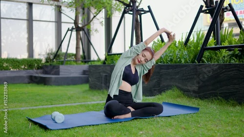Engaging in a calming yoga session, Adult asian woman sitting on mat stretches her muscles and raises her hands towards the sky. Surrounded by greenery, she enjoys the serenity of her routine