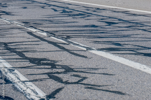 Patches of dark tar repairs crisscross a gray asphalt road, creating a textured pattern and highlighting ongoing road maintenance.