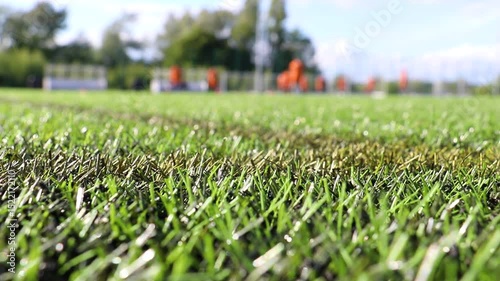 Close up of artificial grass on astroturf sports field. Orange kit players blurred in distance.