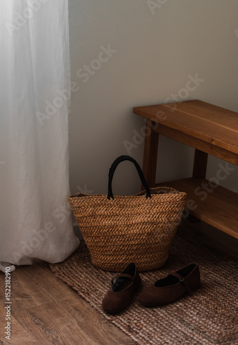 A straw bag on a wooden bench, suede shoes on a jute rug in the hallway. Cozy house concept