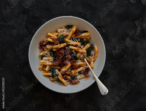 Quick pasta recipe - casarecce with spinach and bacon on a dark background, top view
