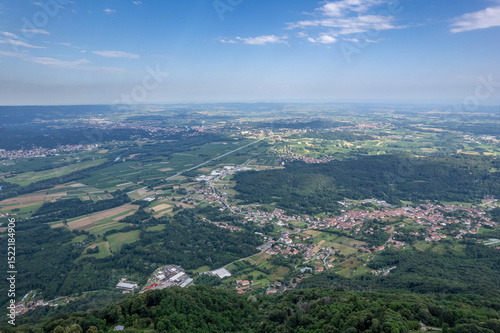Drone panorama of the Ivrea Morainic Amphitheatre seen from Brosso, Val Chiusella, Italy, showing lush green plains, woods, and scattered villages under clear sky, high drone shot, slow motion
