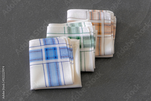 Set of folded handkerchiefs with a striped design is placed on a dark stone surface.