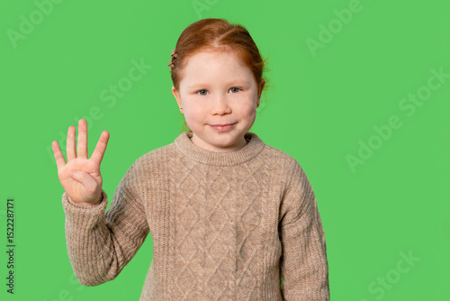 Fototapeta Young girl poses with a cheerful smile while holding up four fingers showing num