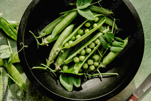 Fresh green peas in pods and beans in a black bowl