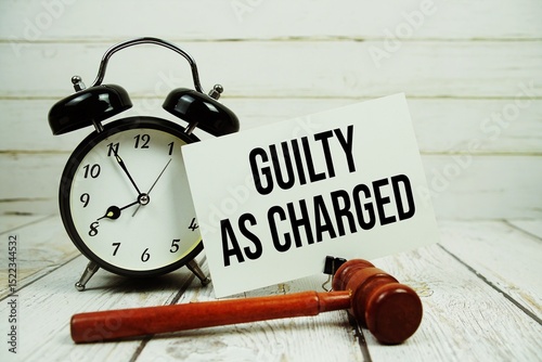 Guilty As Charged text on paper card with alarm clock and wooden judge gavel on wooden background
