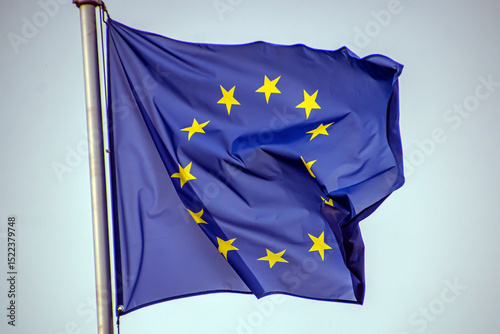 The blue flag of the European Union flutters in the wind against a cloudy grey sky