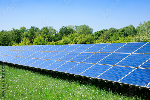 A modern solar plant in a green landscape and trees in the background show the progress of sustainable energy production and the transition to ecologically renewable energy - Munich, Germany