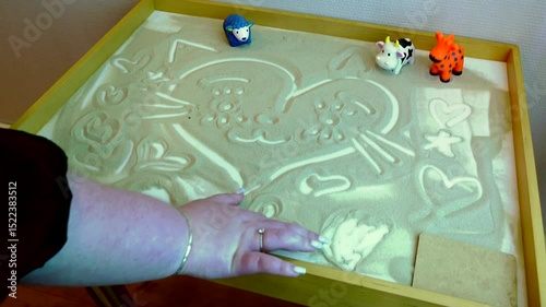 A woman's hand draws cute pictures with sand at a children's center