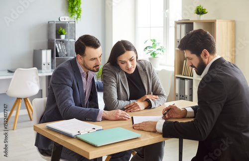 Agent showing contract to couple, business meeting, negotiation, client consultation around desk engaged in discussion, meeting, agent suggesting document for couple in professional office environment