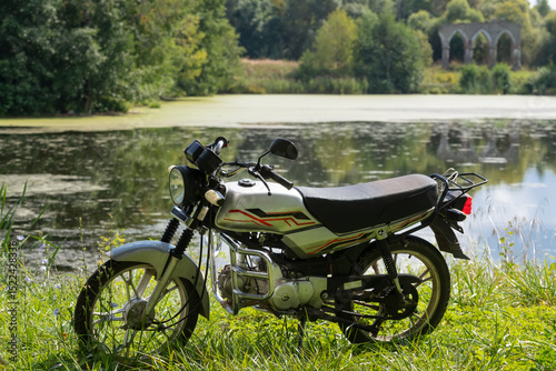 A motorcycle rests on the shore of a pond overgrown with duckweed