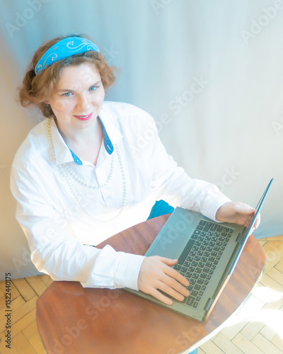 A beautiful young woman is working or playing or shopping on a laptop in a stylish white shirt and a hair band in the shape of the Russian national kokoshnik headdress
