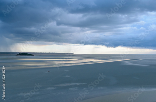 Distant rain patches on the horizon over a serene tidal zone at dusk during low tide