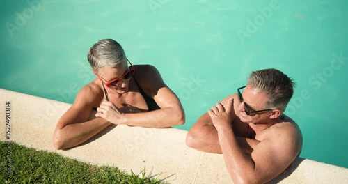 Mature couple relaxing in pool, enjoying conversation and sunshine together
