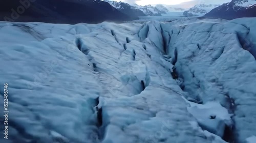 Aerial View of a Glacier's Surface with Deep Crevasses and Mountain Backdrop