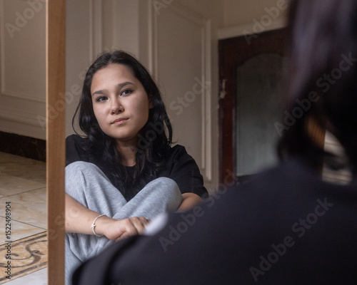 Asian girl sitting thoughtfully in front of mirror photo