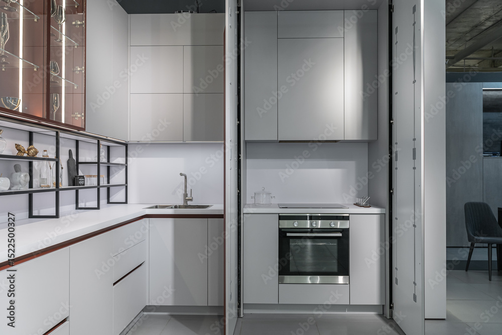 Fototapeta premium large modern built-in kitchen with lots of upper and lower cabinets, drawers and shelves. light countertop, beautiful wine glasses, glass doors, steel faucet and sink. luxury kitchen design.
