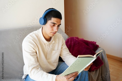 Young man reading and listening to music at home
