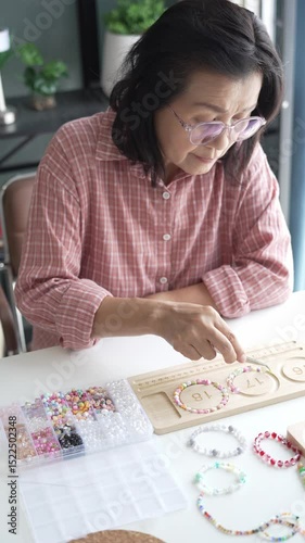 Mature asian woman making handmade jewellery accessories handcraft hobby.