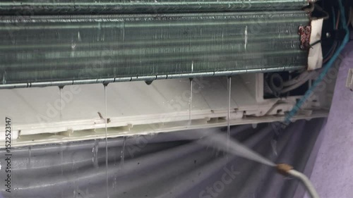 Repairman cleans air conditioner using water stream, close up.