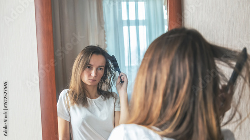 Young woman brushing hair brush looking at the mirror at bedroom